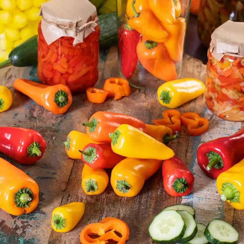 Red and Orange Santa Fe Grande pepper on a table, surrounded by jarred peppers. | copyright: Floramedia UK Ltd