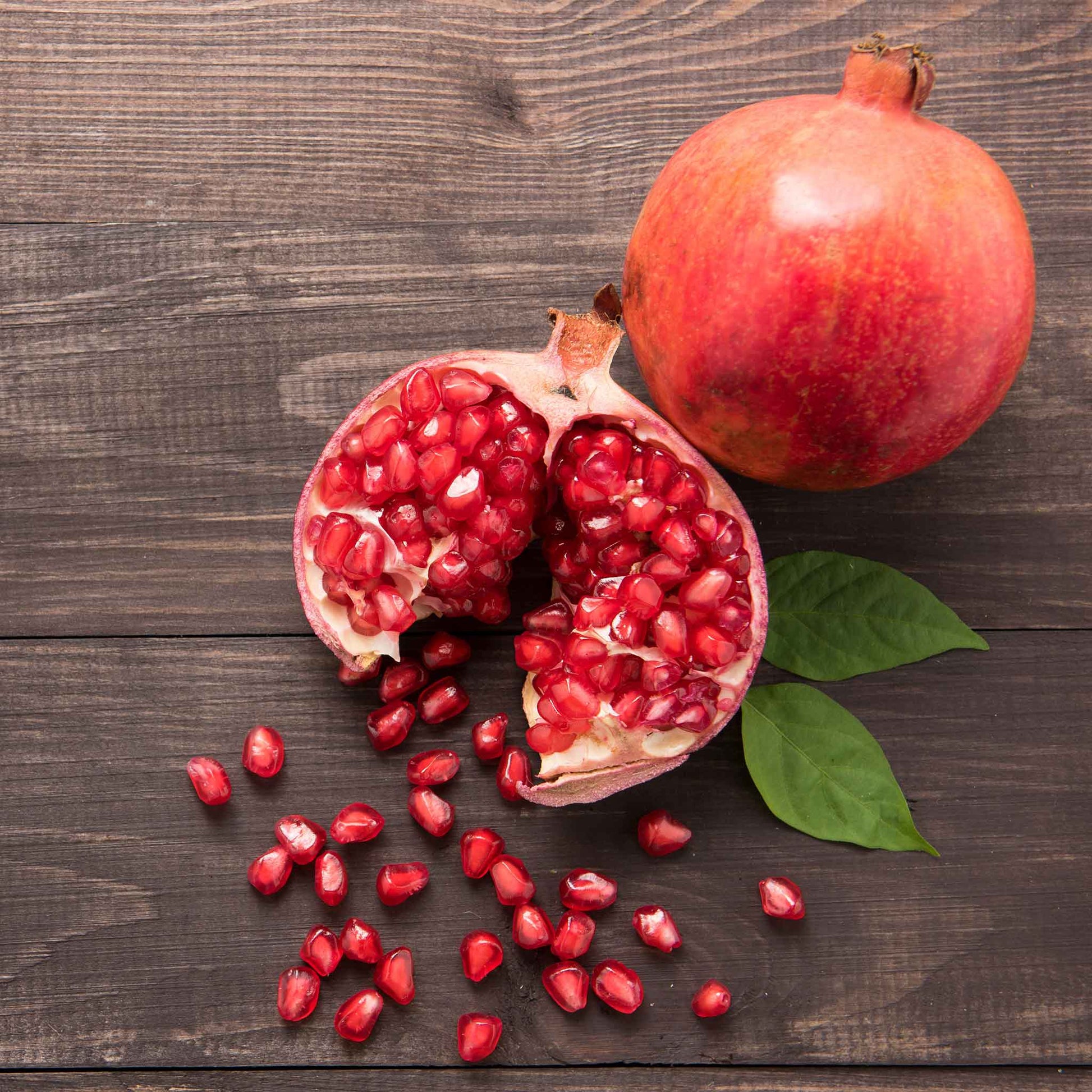 A hand holds a freshly picked, ripe pomegranate, showcasing its vibrant red skin and spherical shape.