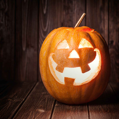 A carved Jack O'Lantern pumpkin with a toothy grin, glowing from within on a dark background.