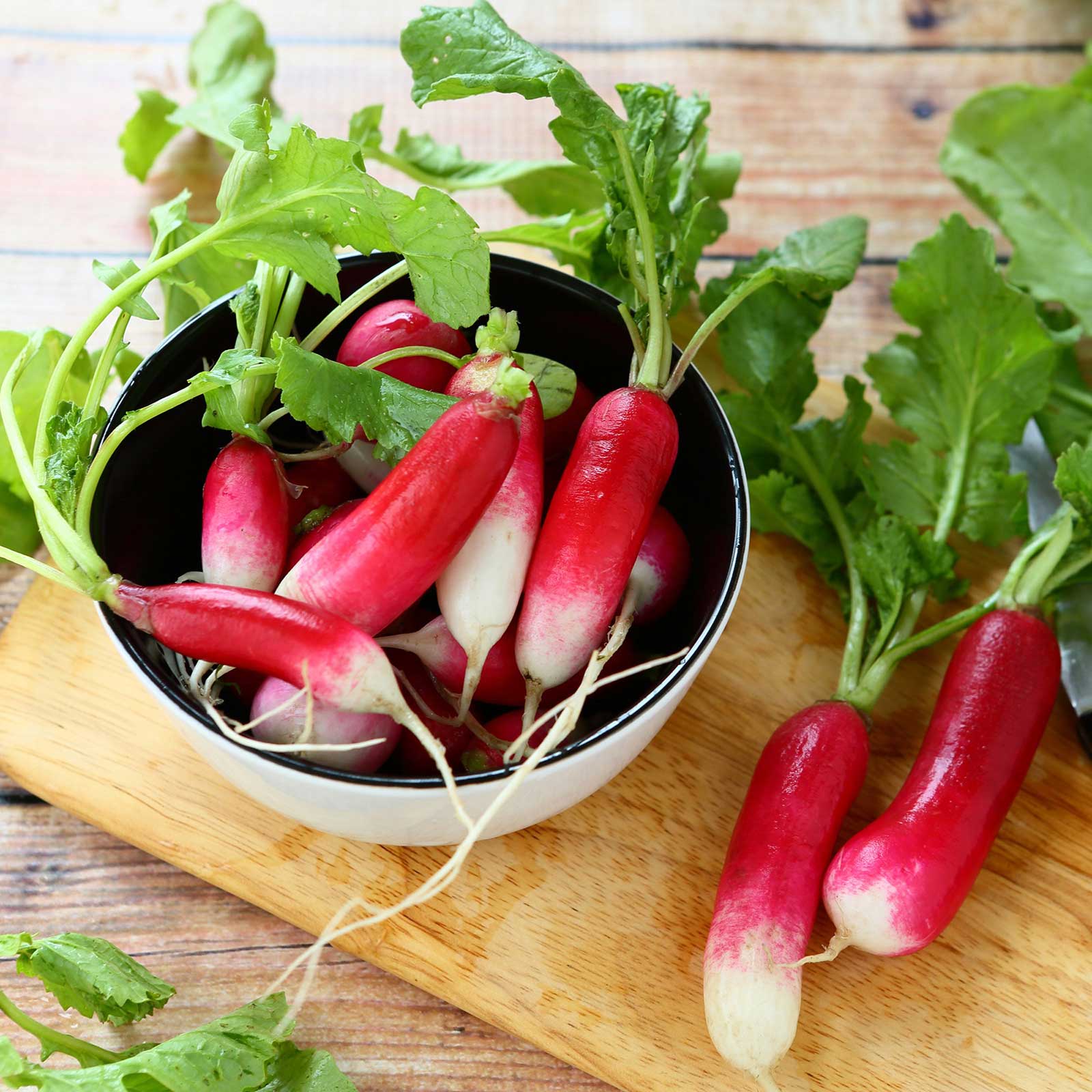 A bunch of French Breakfast radishes with elongated, cylindrical roots, some in a bowl.