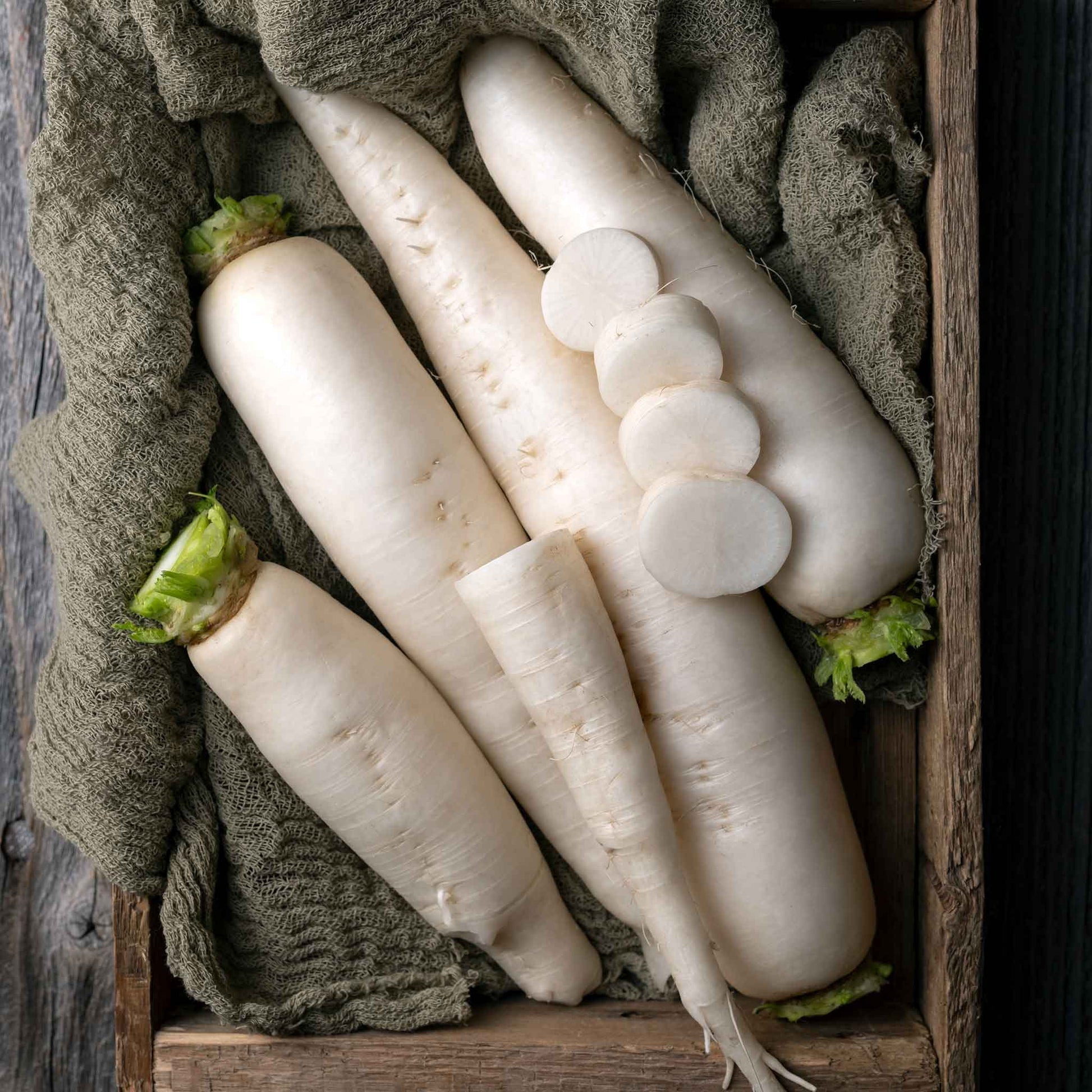 Several large, white Japanese Minowase Daikon radishes are shown, some with leafy green tops.