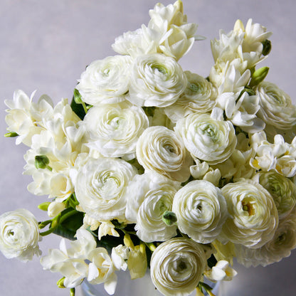 White and yellow ranunculus and freesia flowers with green stems in a garden setting.