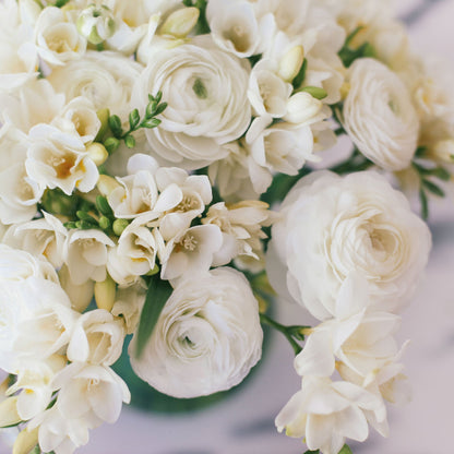 Close-up of three different colors of ranunculus and freesia flowers with green leaves.