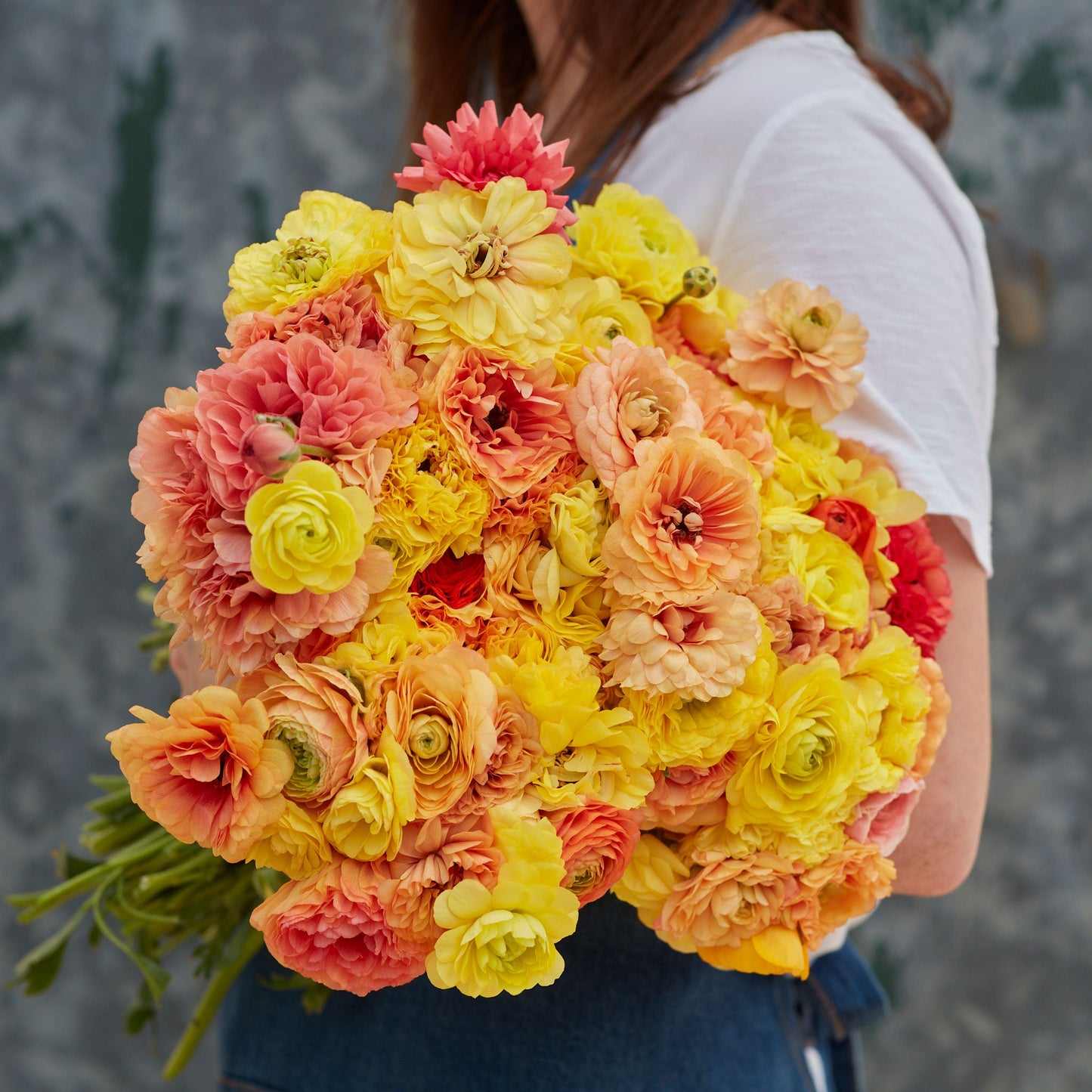 Orange and yellow ranunculus pastel lemon blooms held by a person outdoors