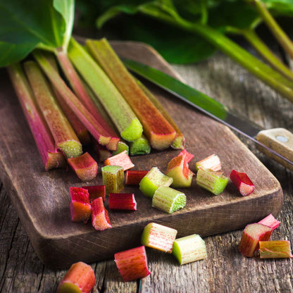 A bunch of Victoria rhubarb stalks with green leaves on a dark surface, cut open revealing the red interior.