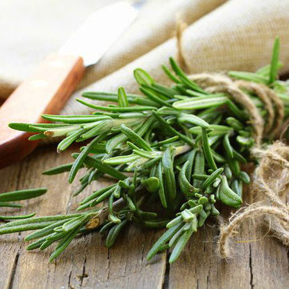 A bundle of fresh rosemary leaves tied together, placed on a wooden surface.