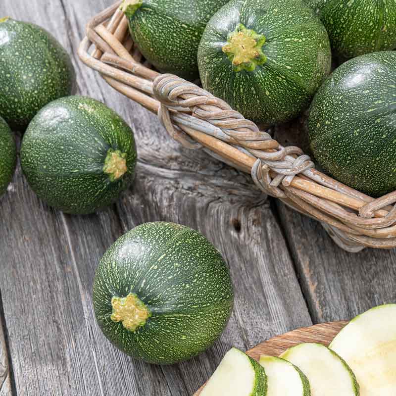 Round Zucchini squash in a basket and on a wooden table. | copyright: Floramedia UK Ltd