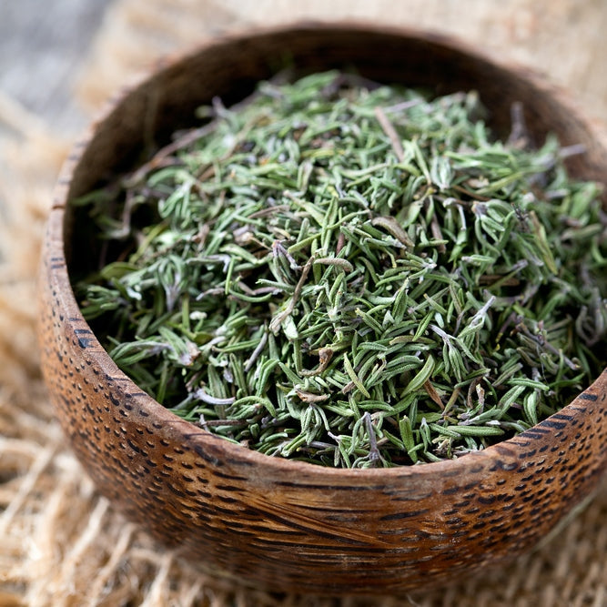 A small wooden bowl filled with fresh, green summer thyme sprigs on a rustic wooden background.