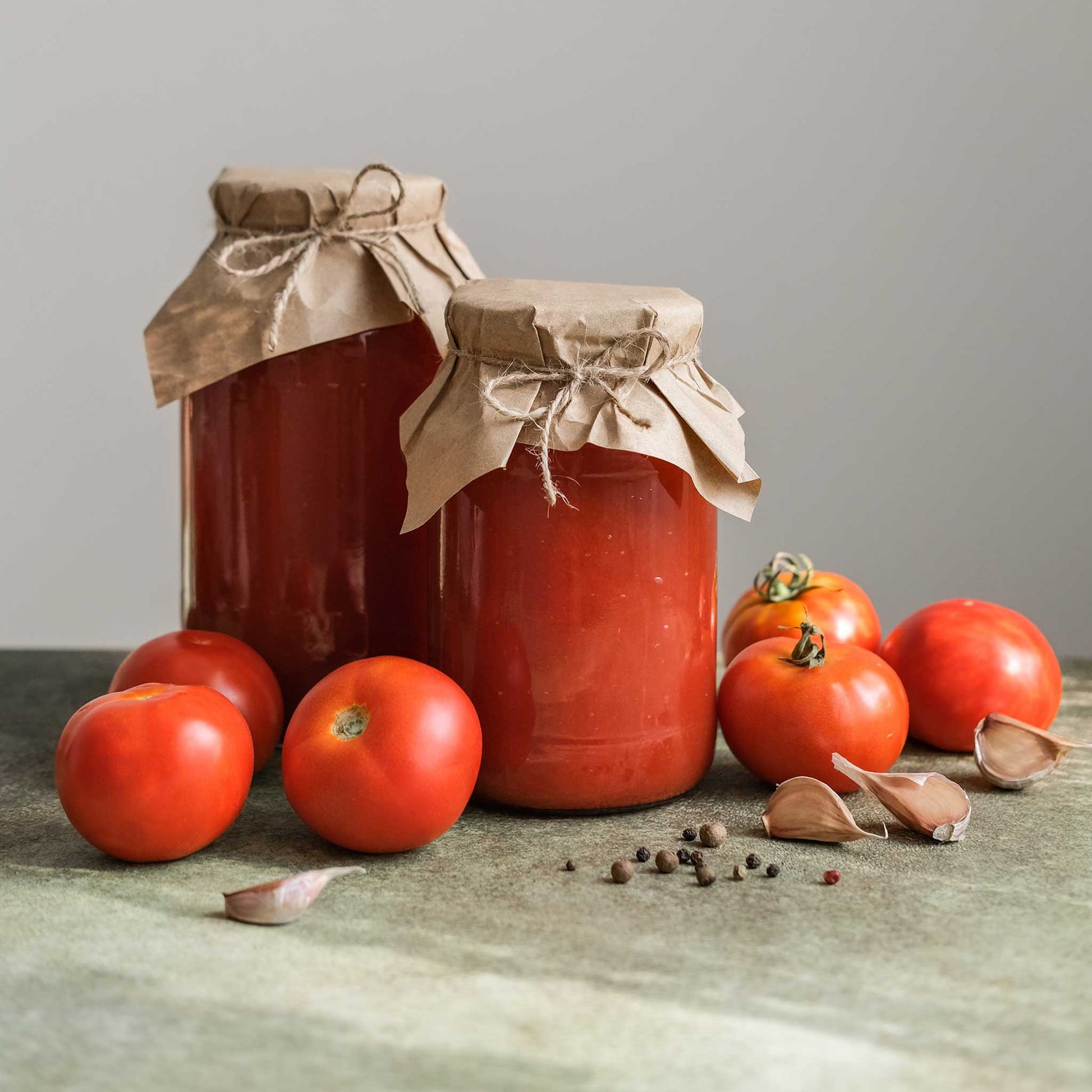 Two jars of tomato sauce with a bow, surrounded by fresh ace 55 tomatoes and garlic on a wooden surface.