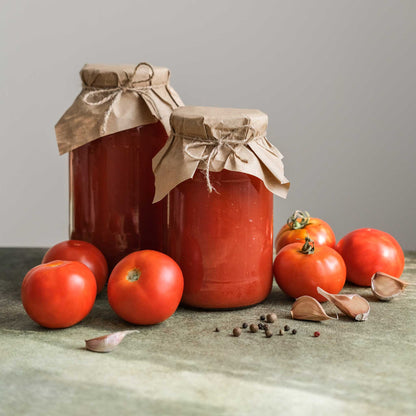 Two jars of tomato sauce with a bow, surrounded by fresh ace 55 tomatoes and garlic on a wooden surface.