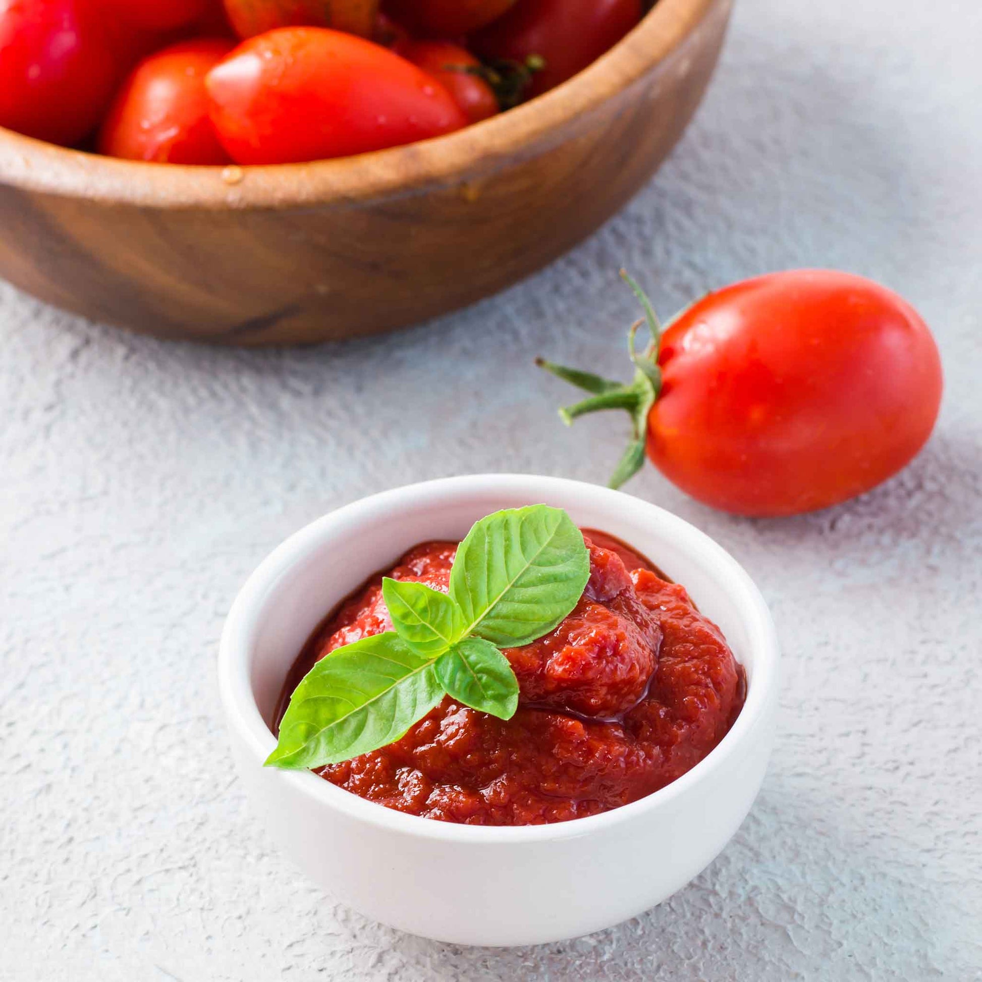 A red Amish Paste tomato next to a bowl of tomato paste.