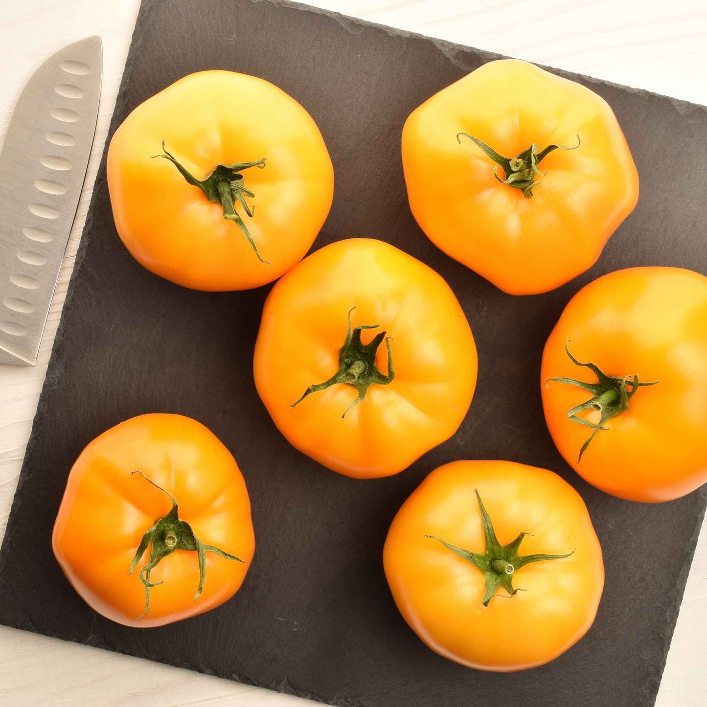 A group of ripe Azoychka tomatoes, yellow with slight red blushing, on a cutting board.