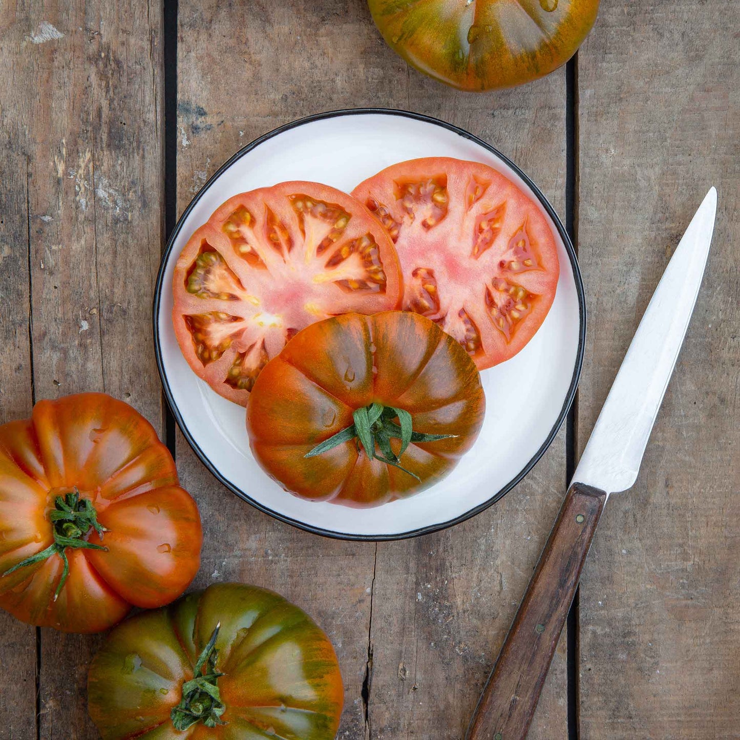 Slices of Black Brandywine tomato with hints of green and brown on its skin, shown on a plate.