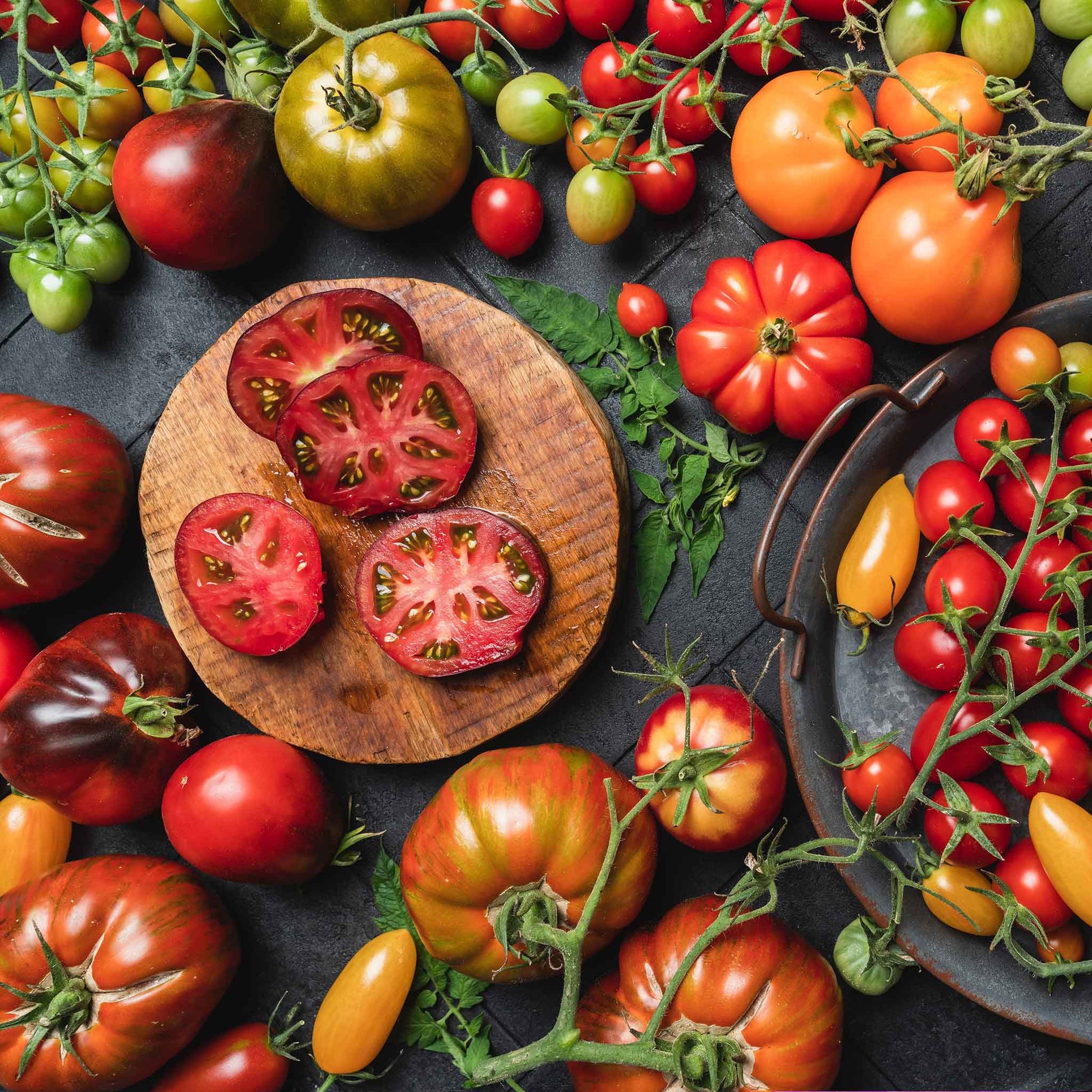 A variety of colorful heirloom tomatoes, including red, yellow, and striped, are displayed on a wooden surface.