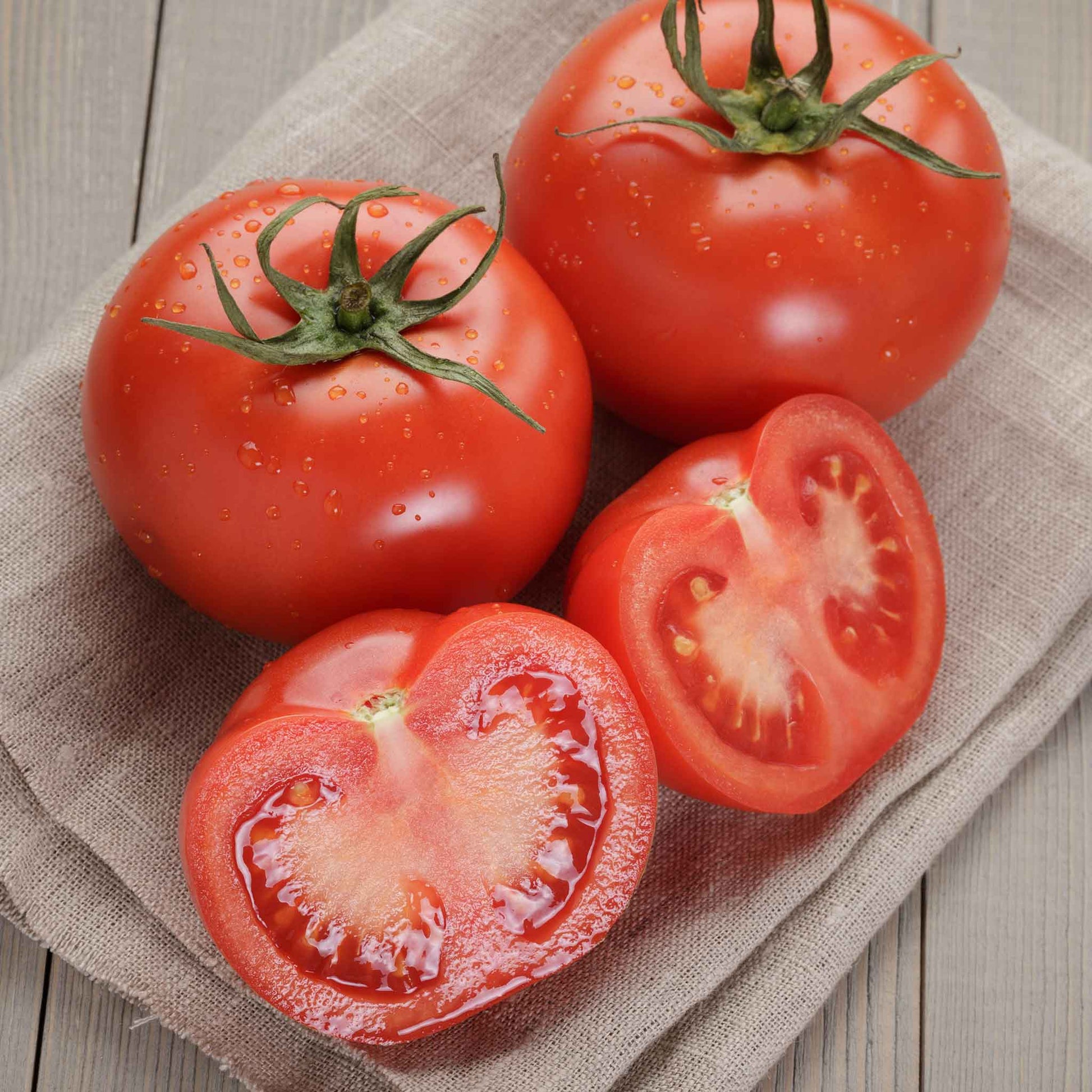 A ripe, red Homestead tomato, sitting on a wooden surface with some sliced tomatoes.