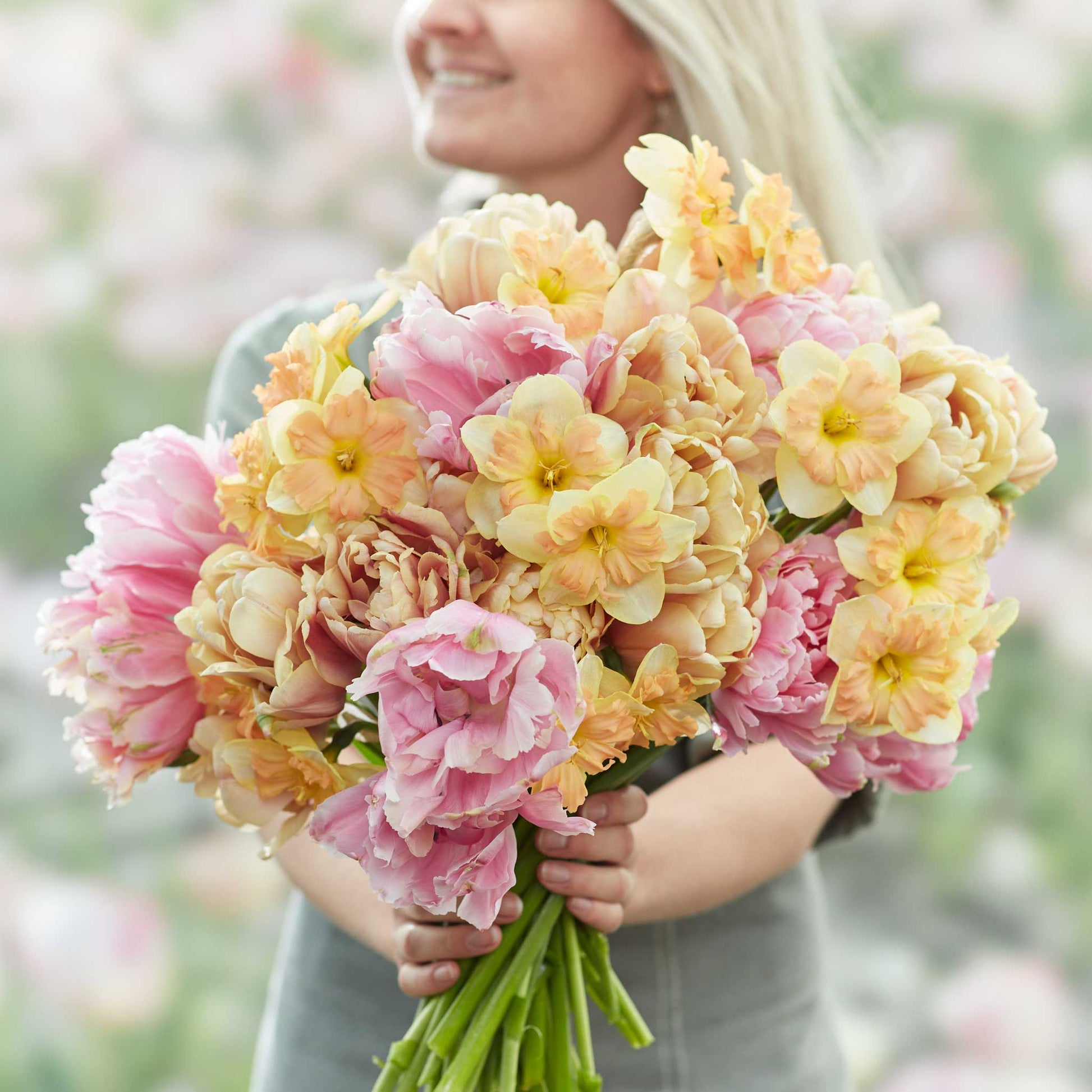 A person holding a vibrant spring garden with pink and purple tulips, and yellow daffodils bouquet.