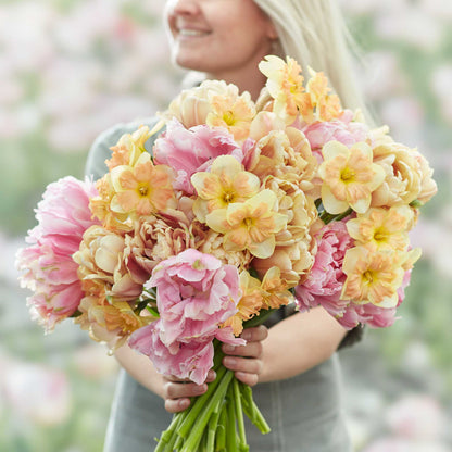A person holding a vibrant spring garden with pink and purple tulips, and yellow daffodils bouquet.