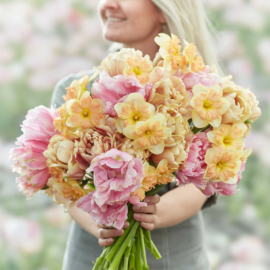 A person holding a vibrant spring garden with pink and purple tulips, and yellow daffodils bouquet.