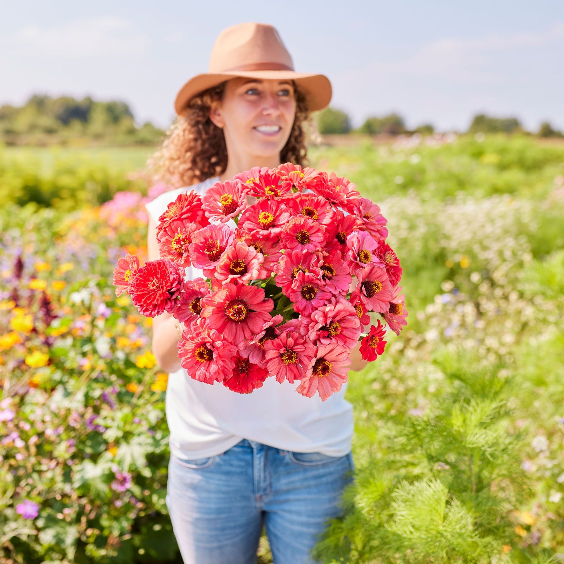 Person holding a bouquet of salmon queen zinnia flowers in a garden setting